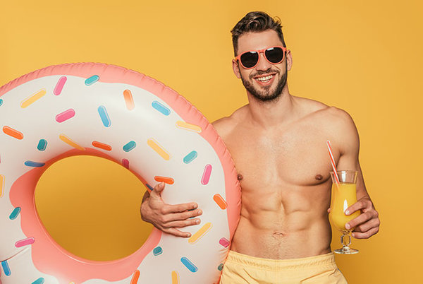 Mann in Badehose mit Schwimmring und Sonnenbrille lacht in die Kamera