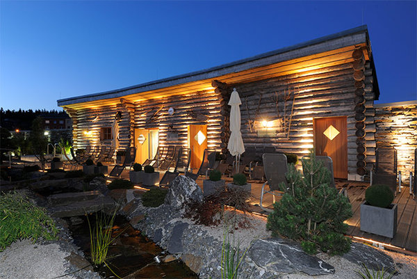 Blick in den abendlichen Saunagarten mit Bachlauf, Liegen und Außengebäude mit Holzfassade